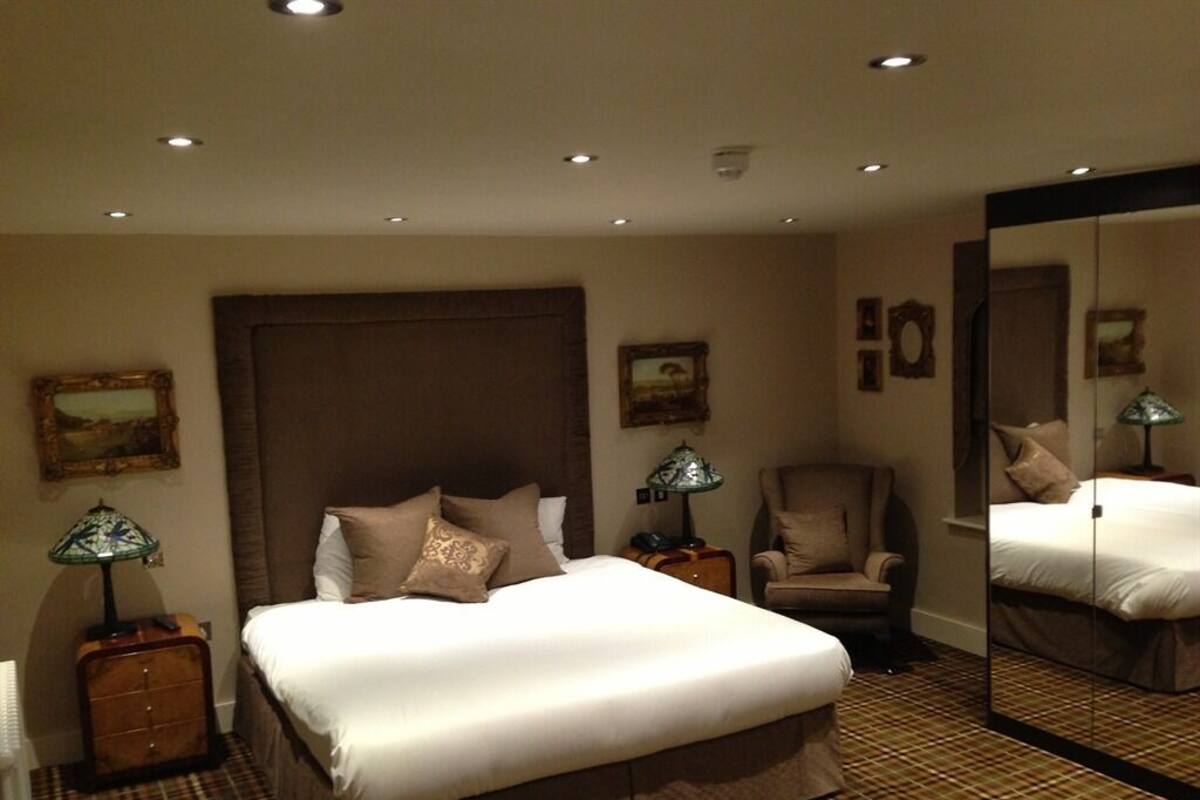 Une chambre d’hôtel avec un grand lit, une chaise, une table de chevet avec une lampe et un miroir.