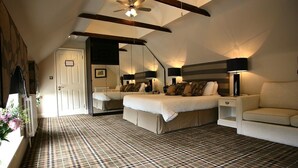 A bedroom with a large bed, a sofa, a nightstand, a ceiling fan, and a radiator. - The White Hart Hotel (Halstead)