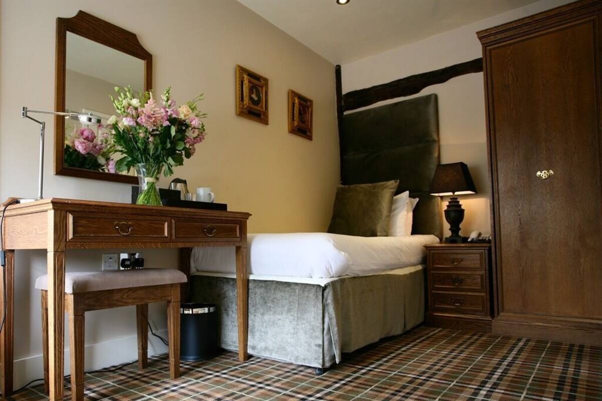 Une chambre à coucher comprenant un lit, une table de chevet, une lampe, une commode, un miroir et un sol à motifs écossais.