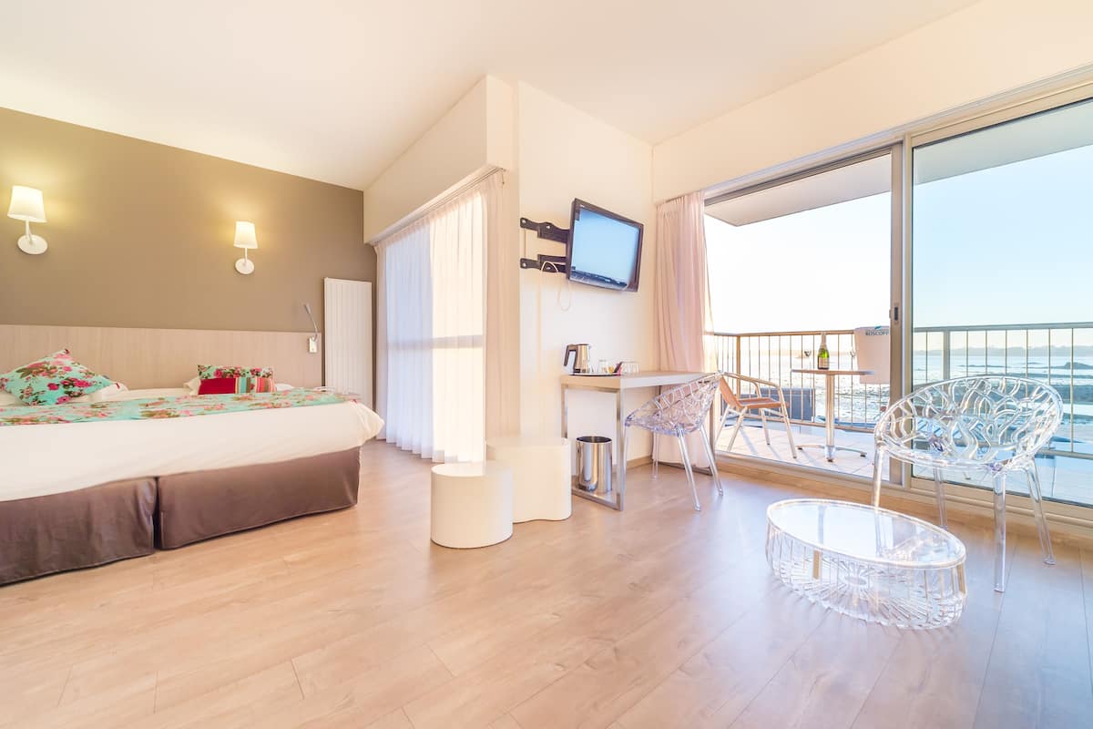 Een hotelkamer met een bed, een televisie, een balkon met stoelen en een kleine tafel.