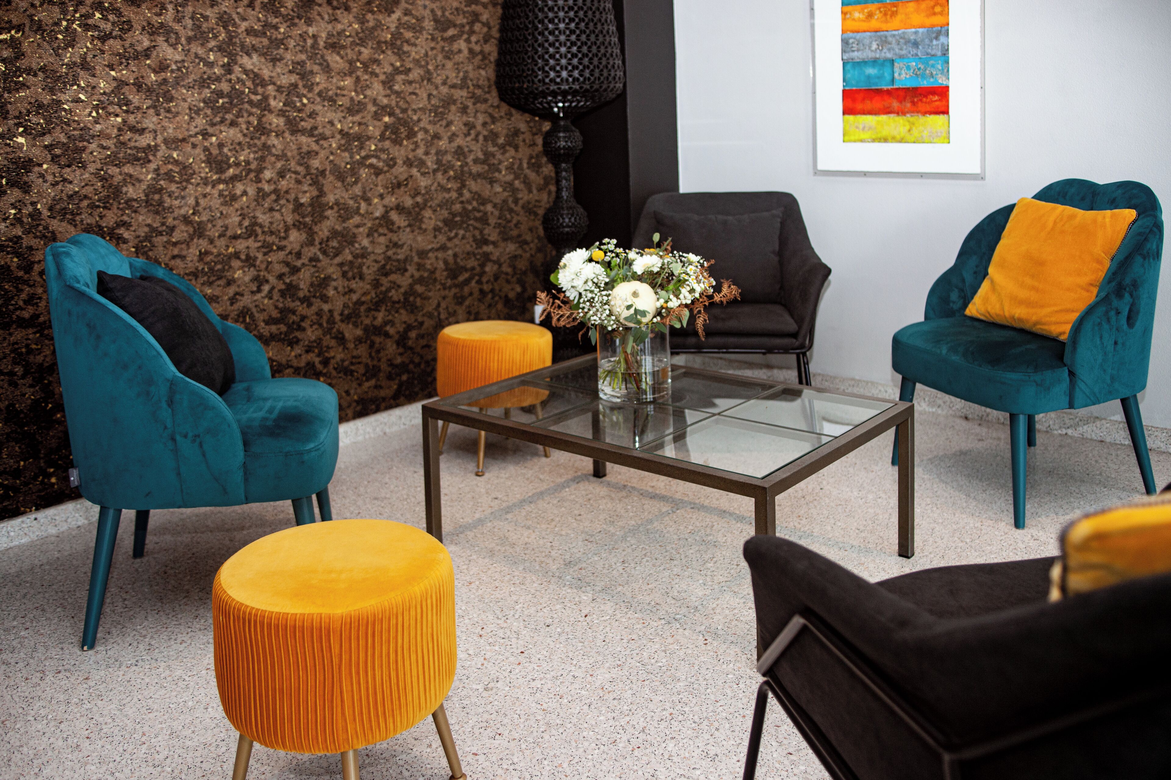 A modern living room with teal and black sofas, a glass coffee table, and a yellow ottoman.