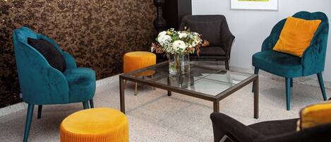 A modern living room with teal and black sofas, a glass coffee table, and a yellow ottoman.