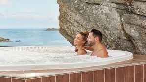 Una pareja en un jacuzzi con un acantilado rocoso y vista al océano.