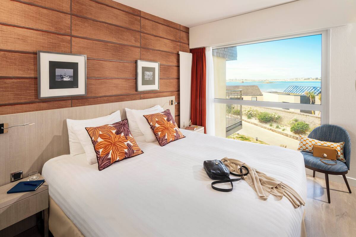 Hotelkamer met een groot bed, uitzicht op het strand en een balkon met een stoel.