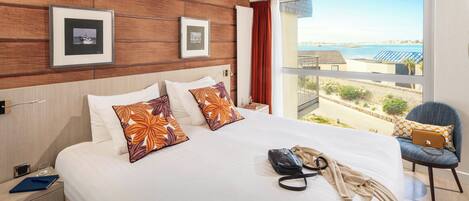 A hotel room with a large bed, a view of the beach, and a balcony with a chair.