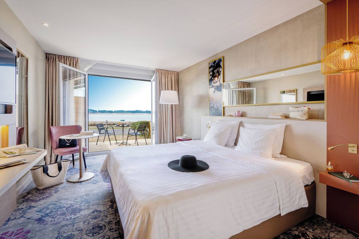 Een hotelkamer met een groot bed, een bureau met stoel, een tafeltje en uitzicht op zee.