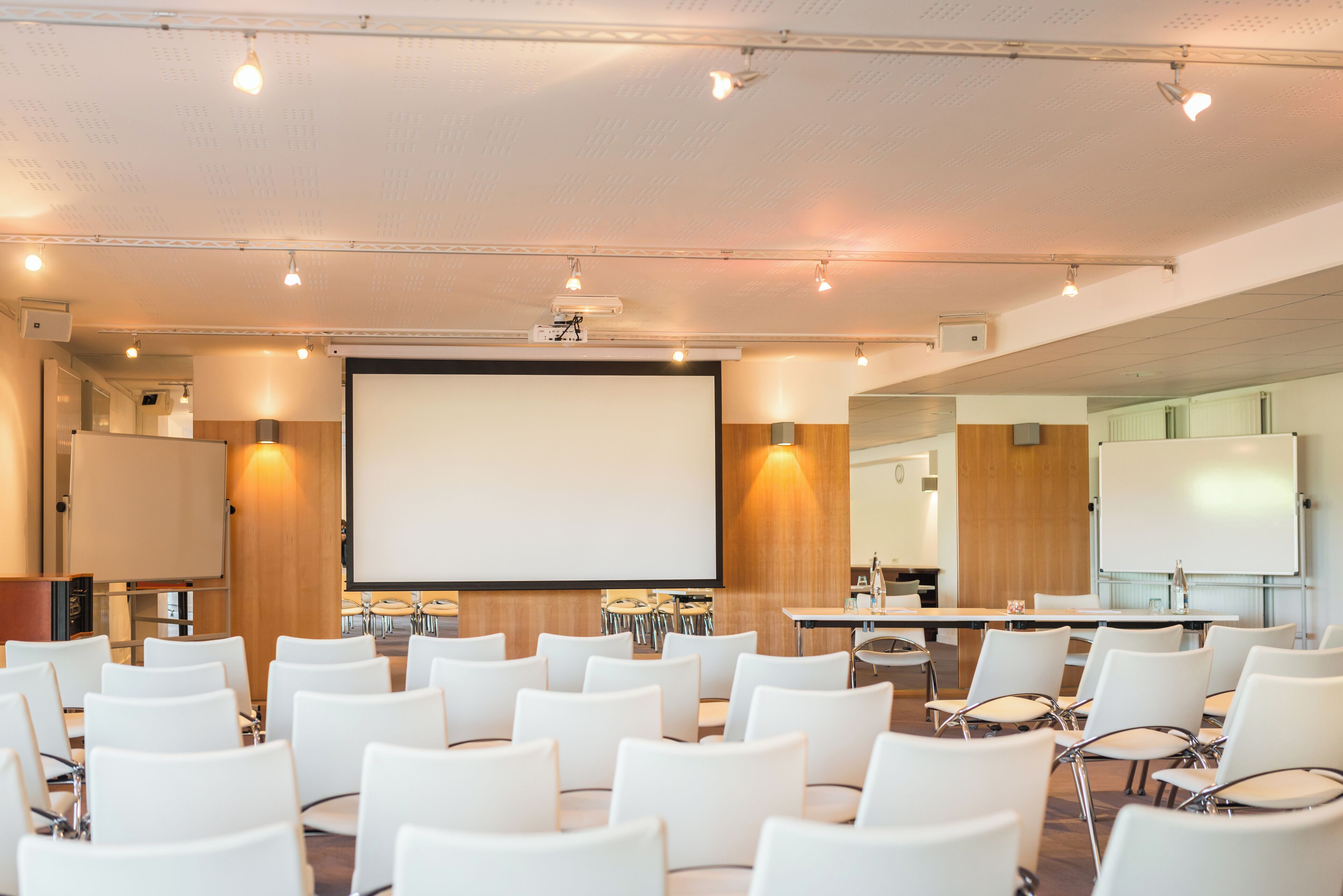 A conference room with white chairs, a large screen, and tables.