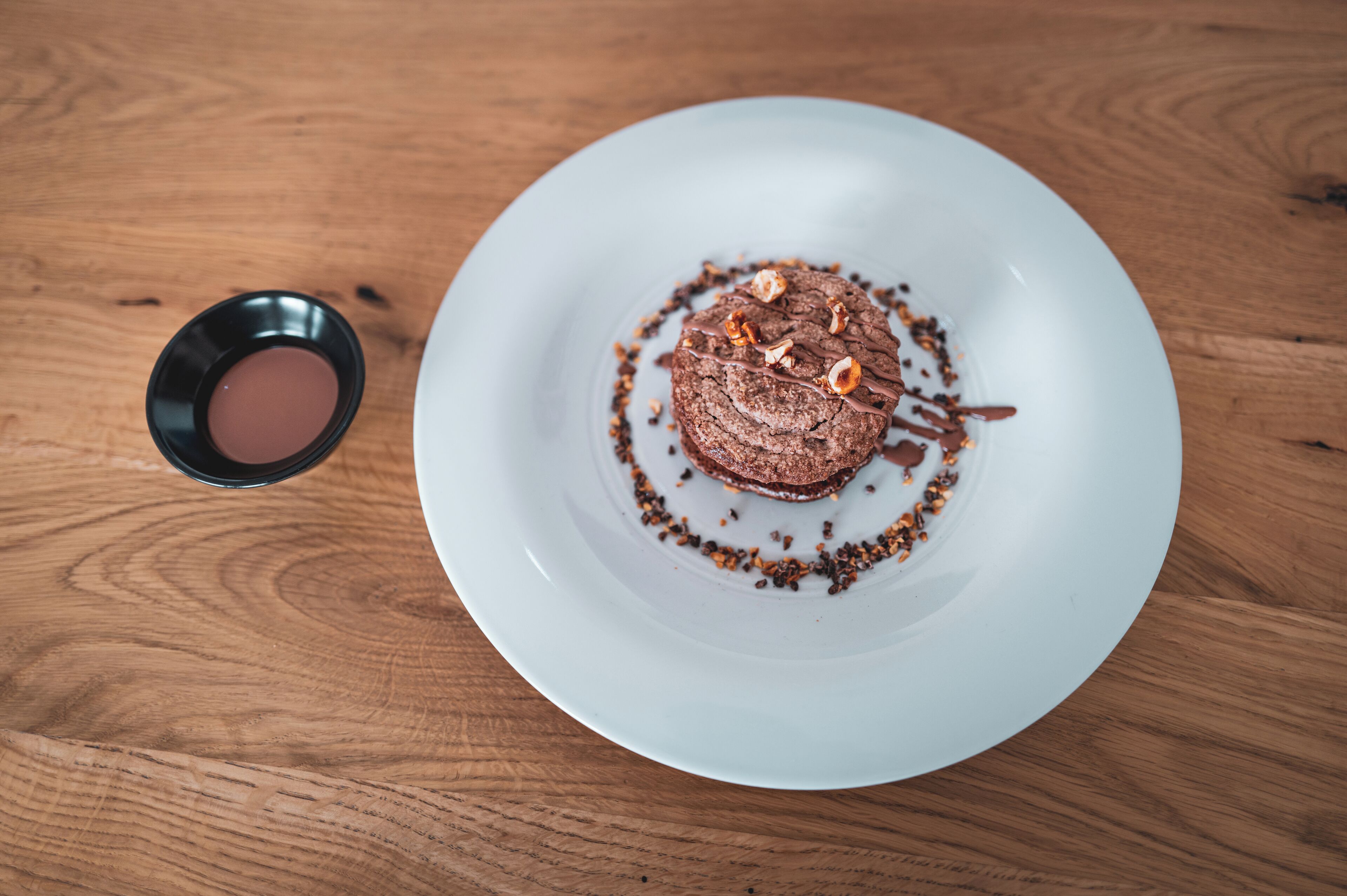 A dessert on a white plate with a small bowl of sauce on a wooden table.