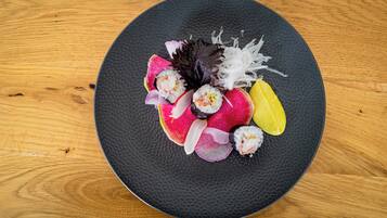 En rund, sort tallerken med forskellige sushi-stykker på et træbord.