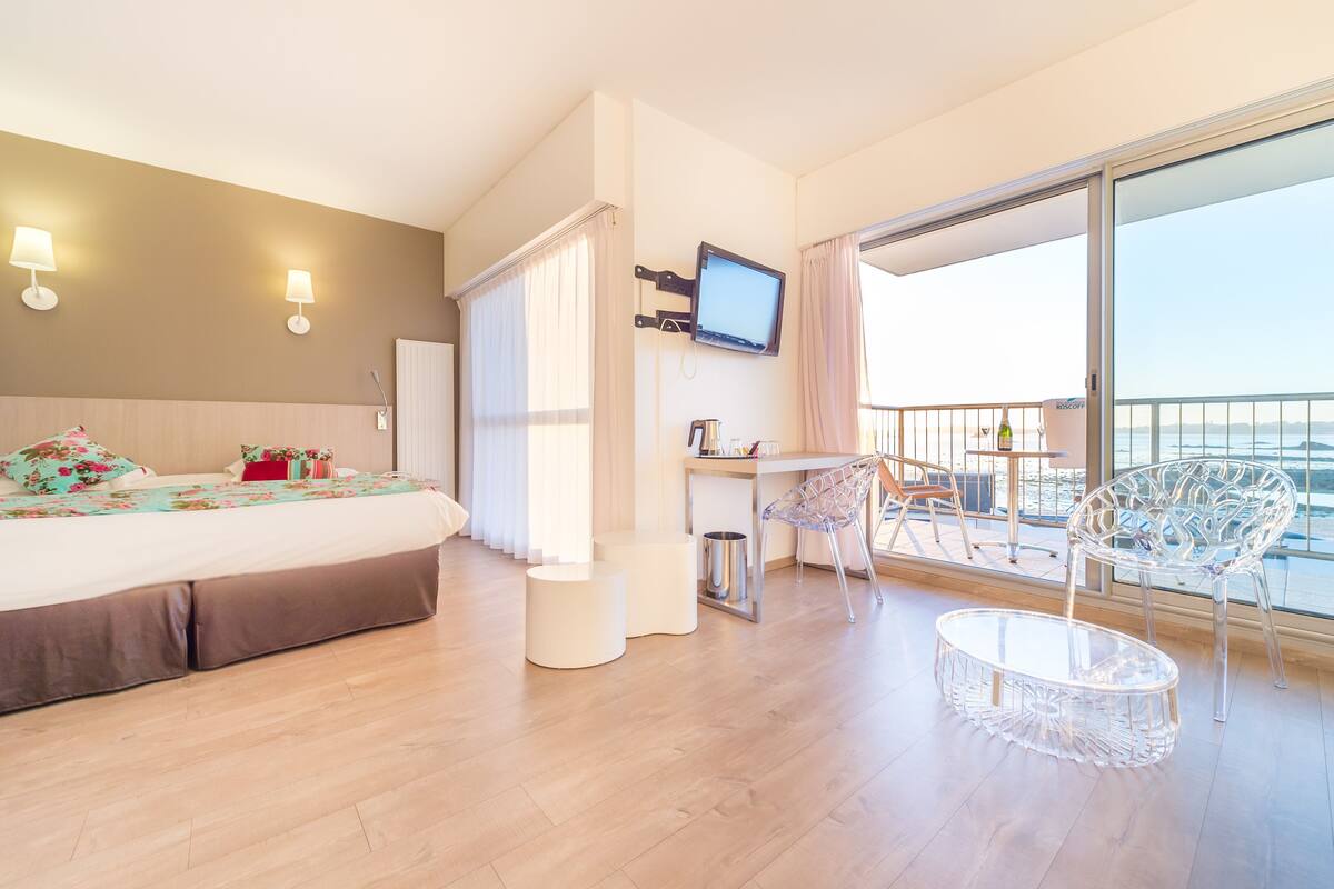 Een hotelkamer met een bed, een televisie, een balkon met stoelen en een kleine tafel.