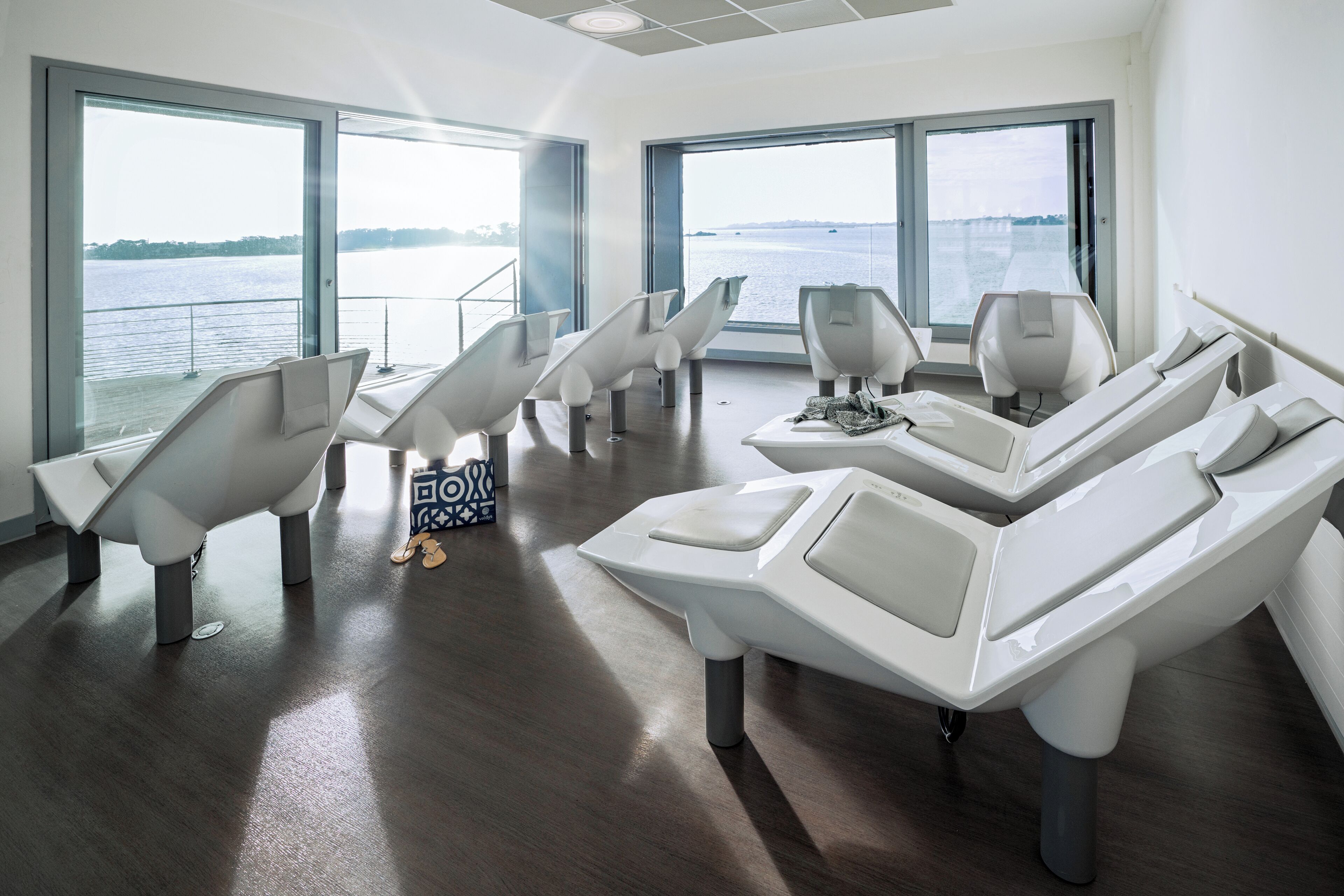 A modern dental clinic with reclining chairs and large windows overlooking a body of water.
