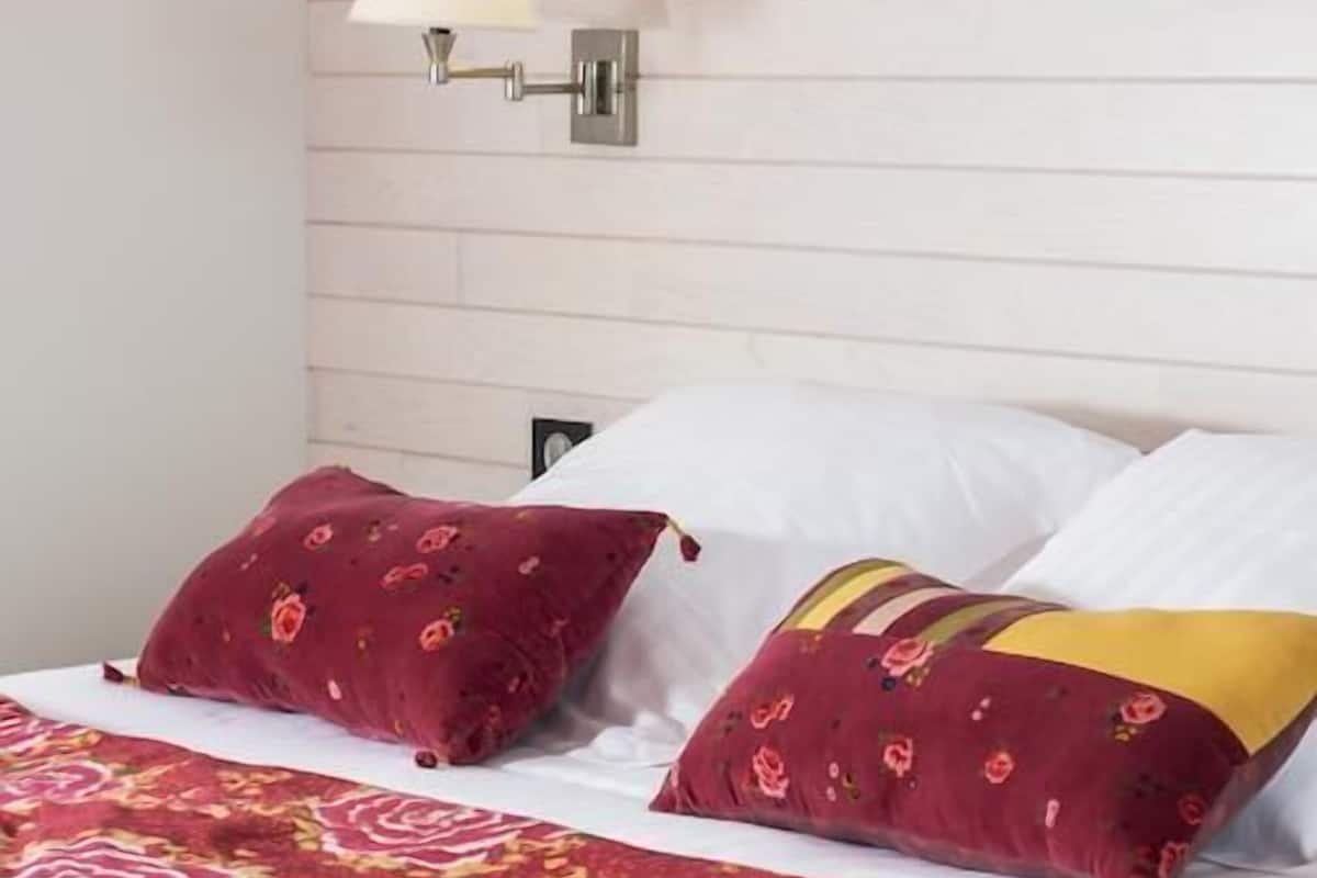 Een bed met een bloemenprint sprei, twee kussens en een wandlamp.