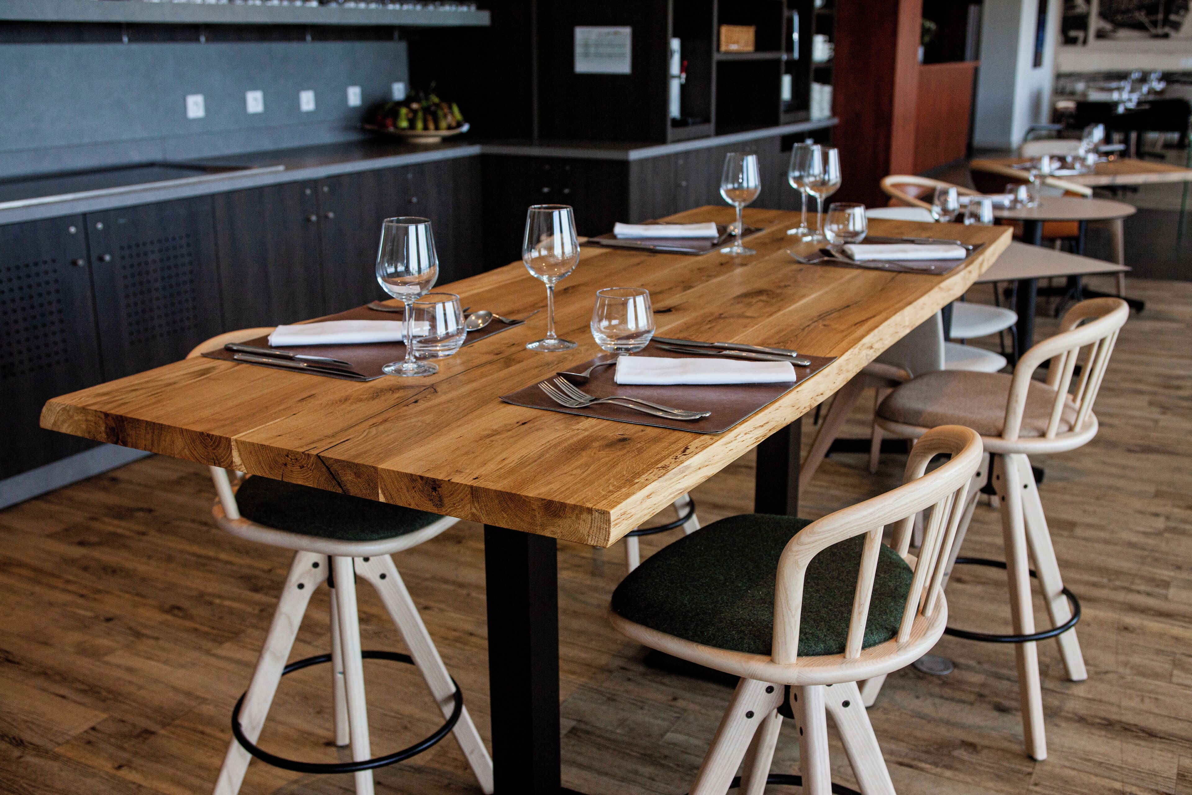 Un restaurante con una larga mesa de madera dispuesta para comer, equipada con copas de vino, cubiertos y servilletas.
