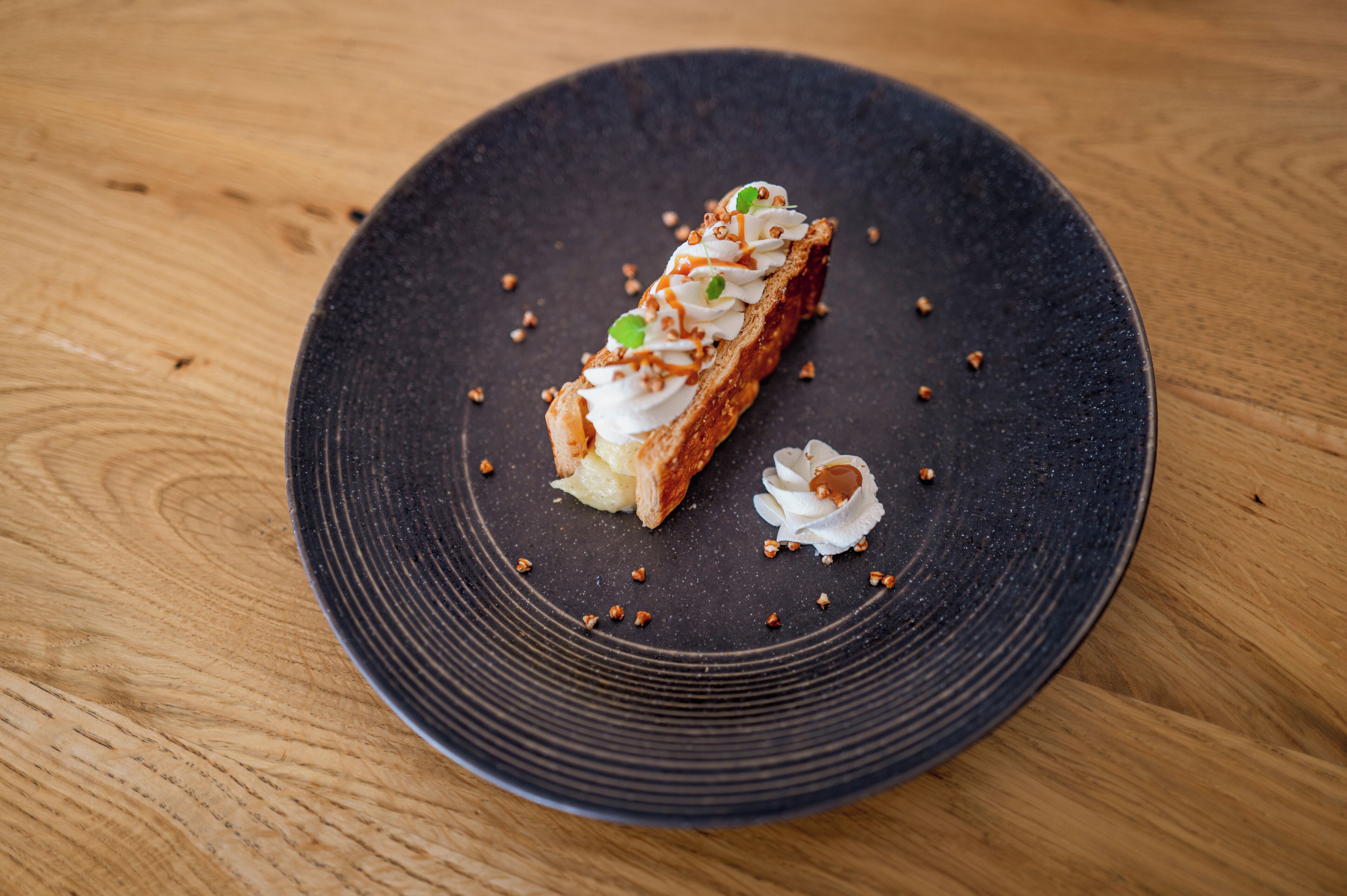 Un postre sobre un plato oscuro, con una mesa de madera de fondo.