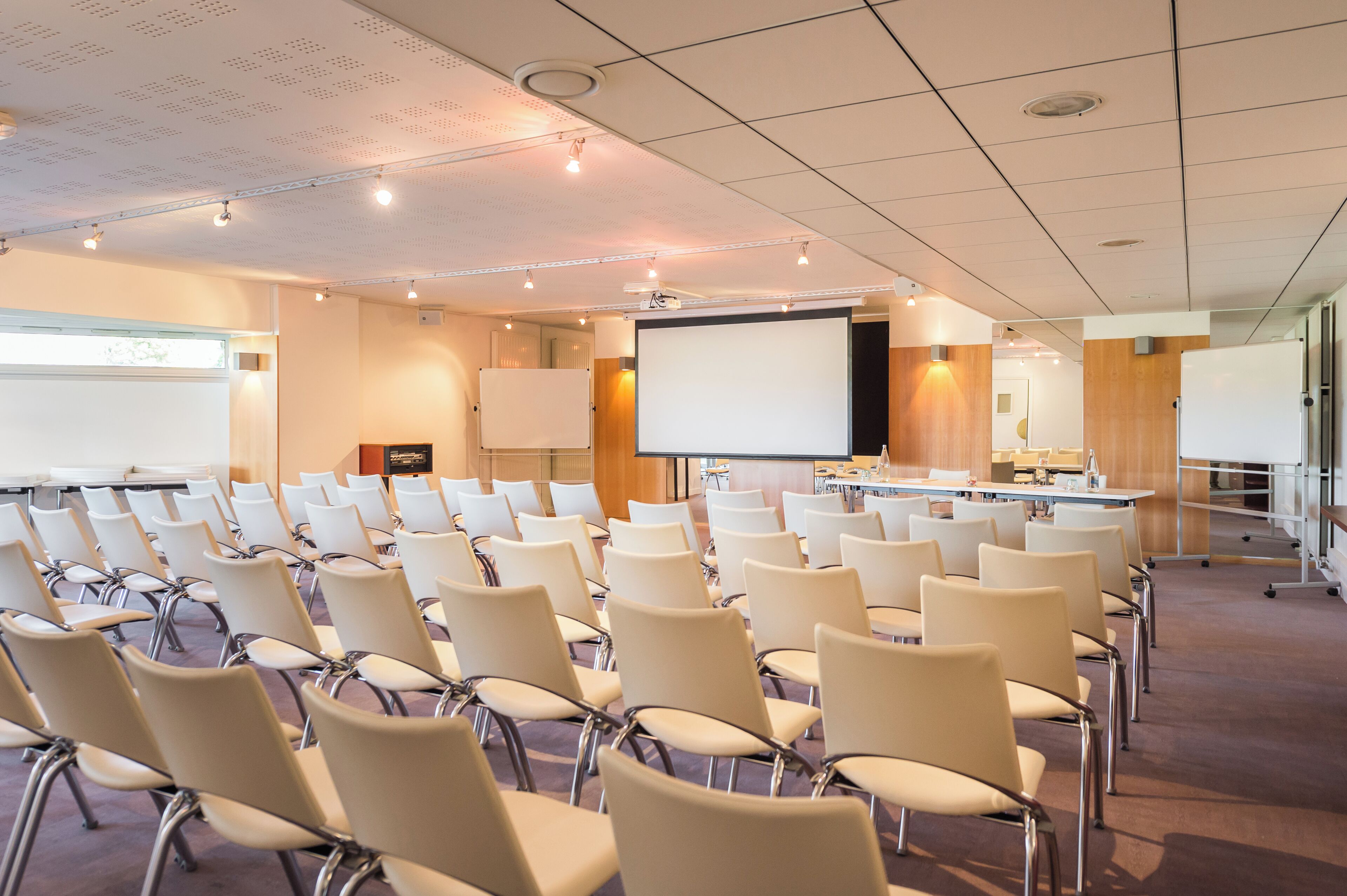 Un salón de conferencias con filas de sillas, una pantalla de proyector y una pizarra.