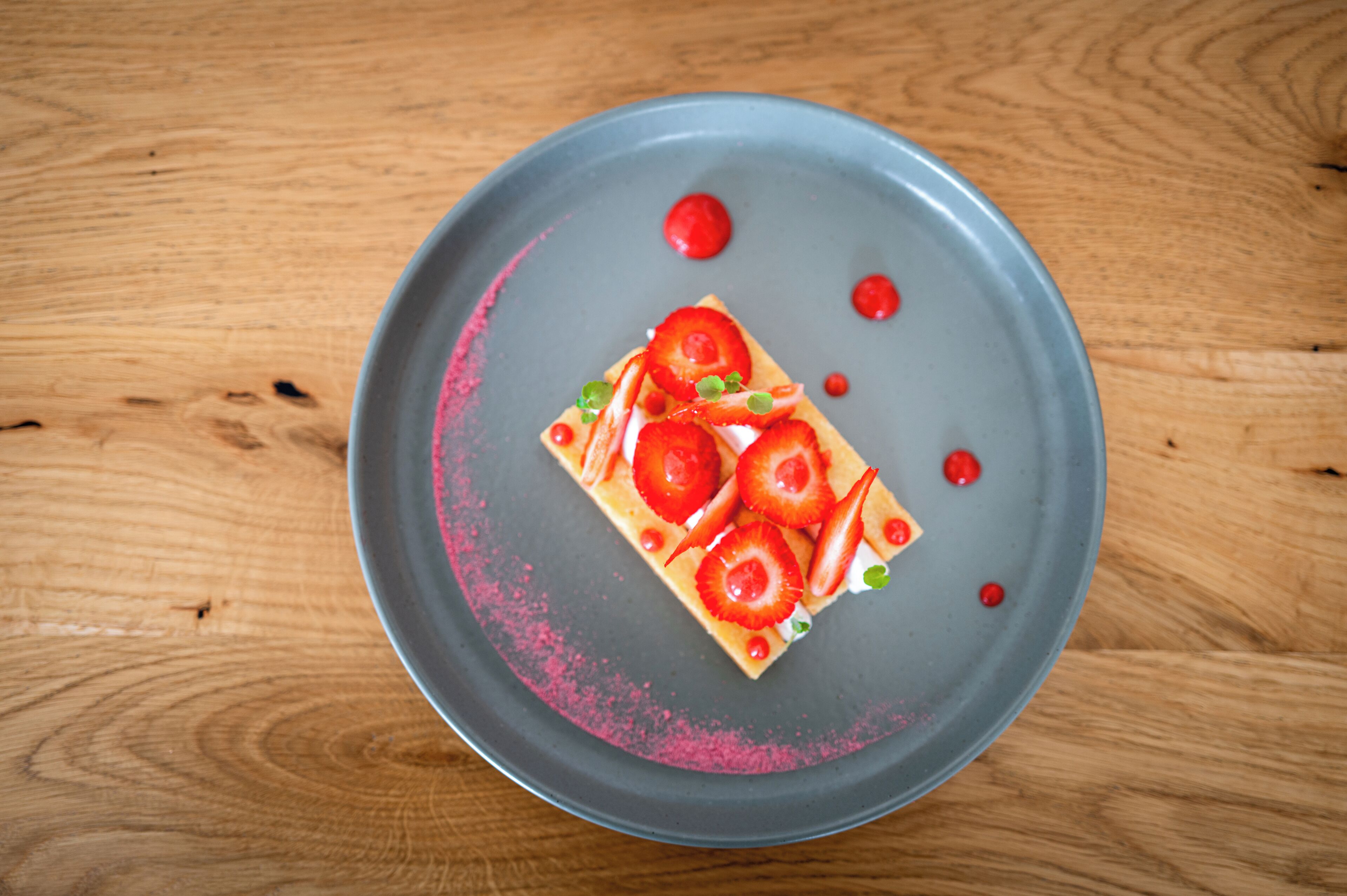Ein rechteckiger Teller mit einer Kuchenstückchen, belegt mit Erdbeeren und einer rosa, puderartigen Schicht.