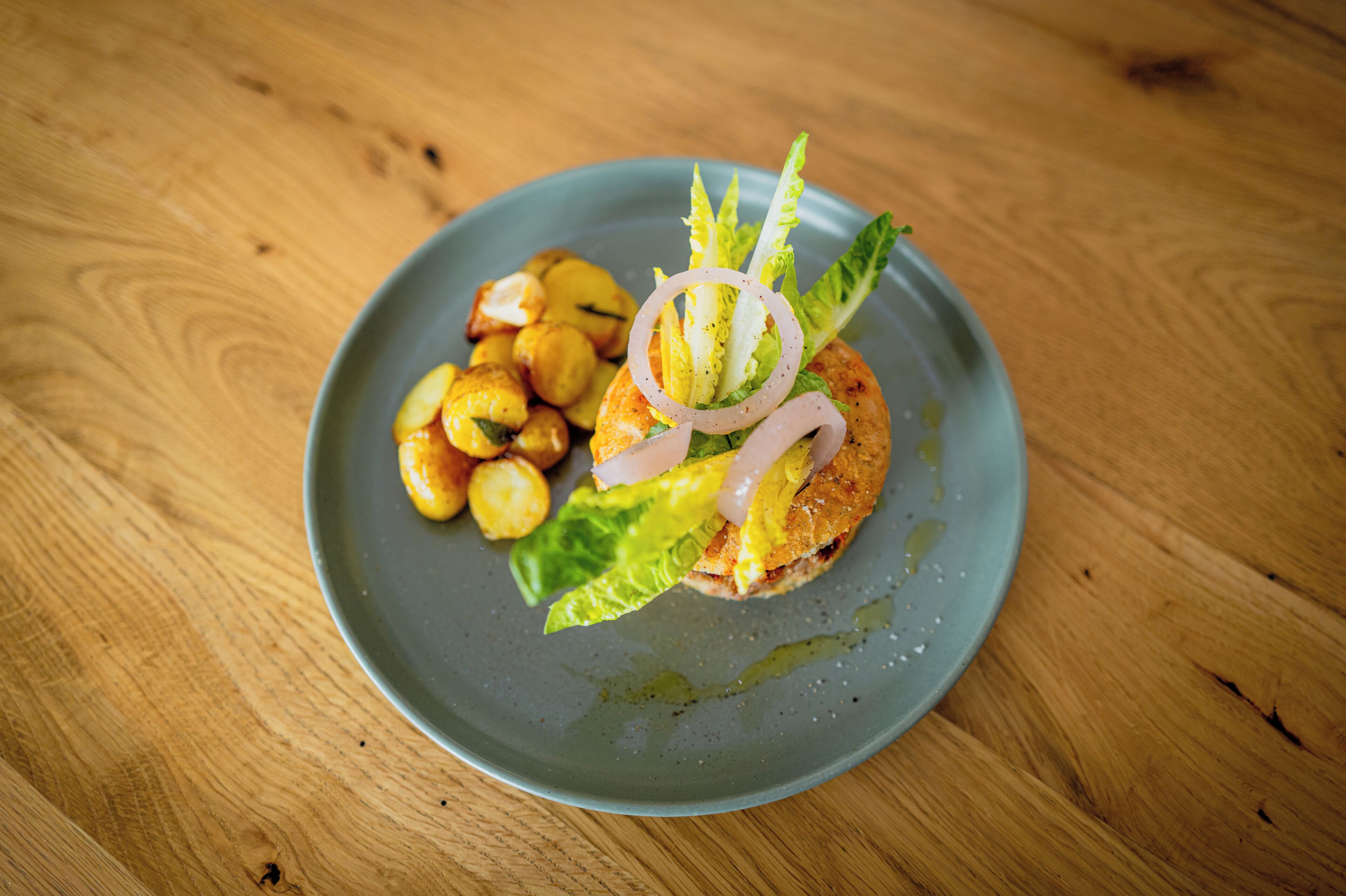 A plate with a sandwich, lettuce, and roasted potatoes on a wooden table.