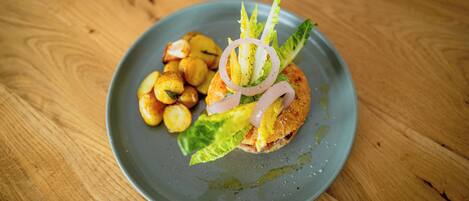A plate with a sandwich, lettuce, and roasted potatoes on a wooden table.