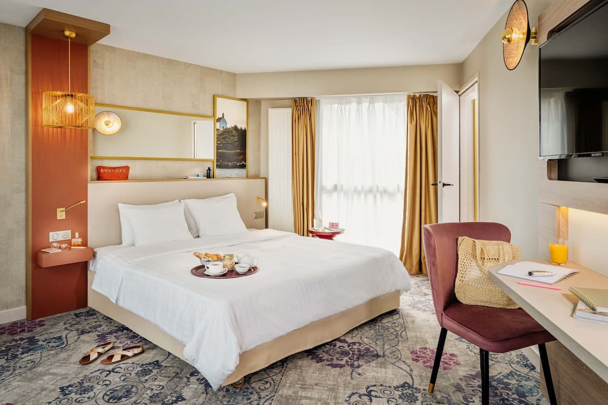 Een hotelkamer met een groot bed, een bureau met stoel, een televisie en een raam met gordijnen.