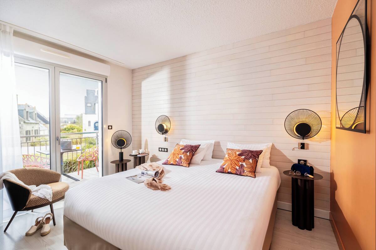 Hotelkamer met een groot bed, twee nachtkastjes, een stoel, een balkon met uitzicht en een schuifdeur naar buiten.