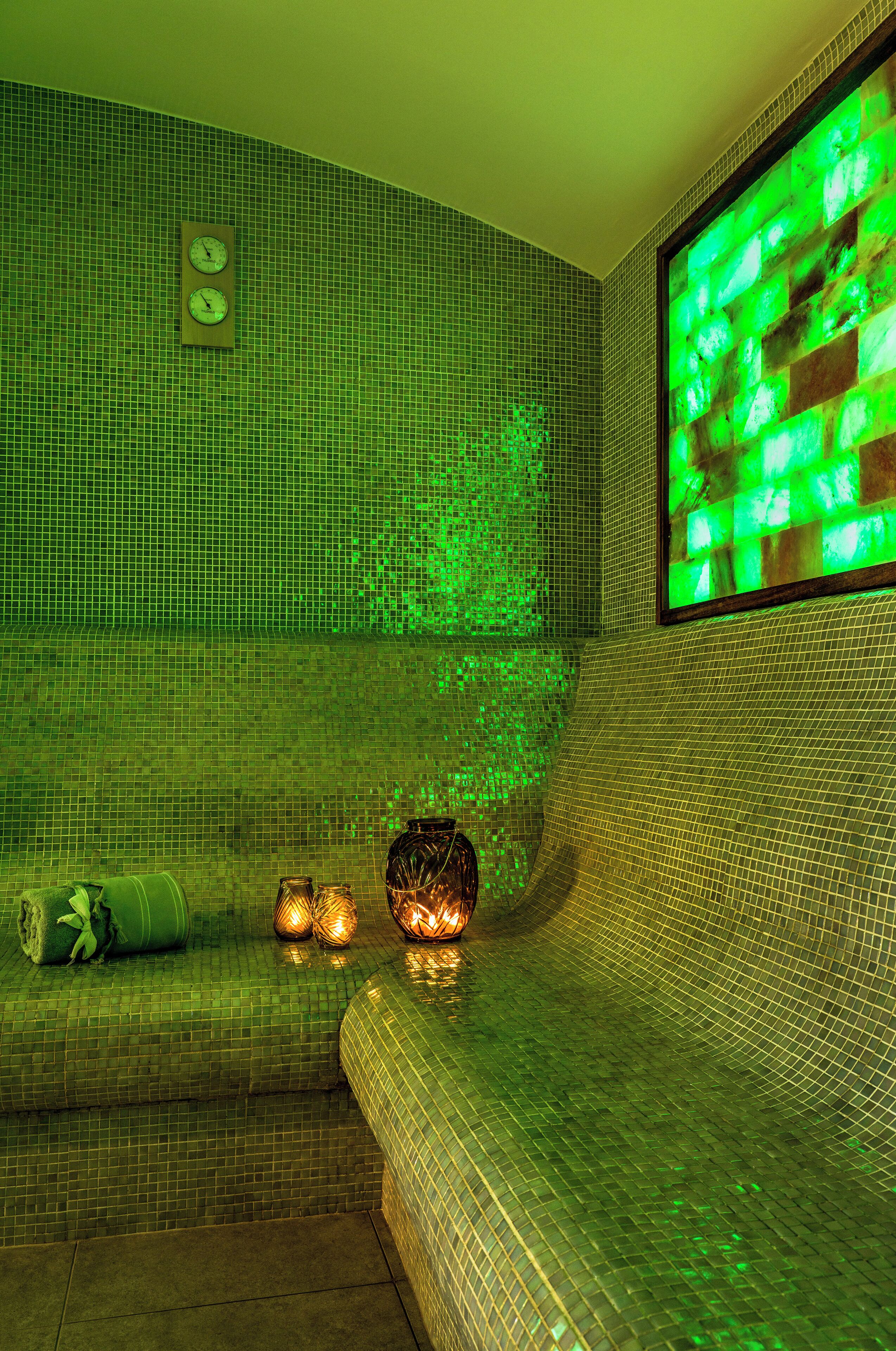 Una stanza spa con un muro rivestito di piastrelle verdi, una sveglia e due candele su una panca.