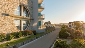 Un edificio moderno con fachada de piedra, varios balcones y un jardín cuidado.