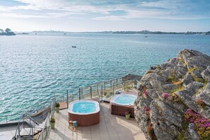 A deck with two hot tubs overlooking a body of water, a staircase, and rocky terrain with vegetation. - Hôtel Valdys Thalasso & Spa - Beau rivage (Roscoff)