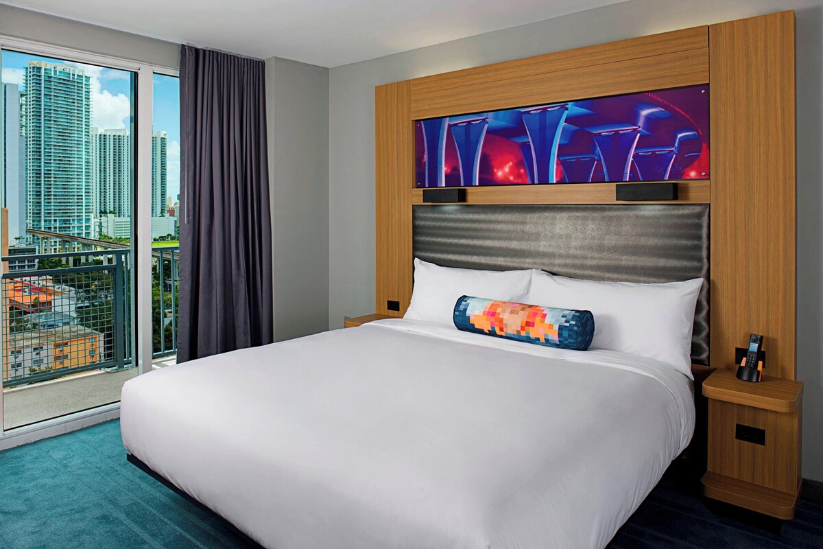 Habitación de hotel con una cama grande, vistas a la ciudad, televisor y cabecero de madera.