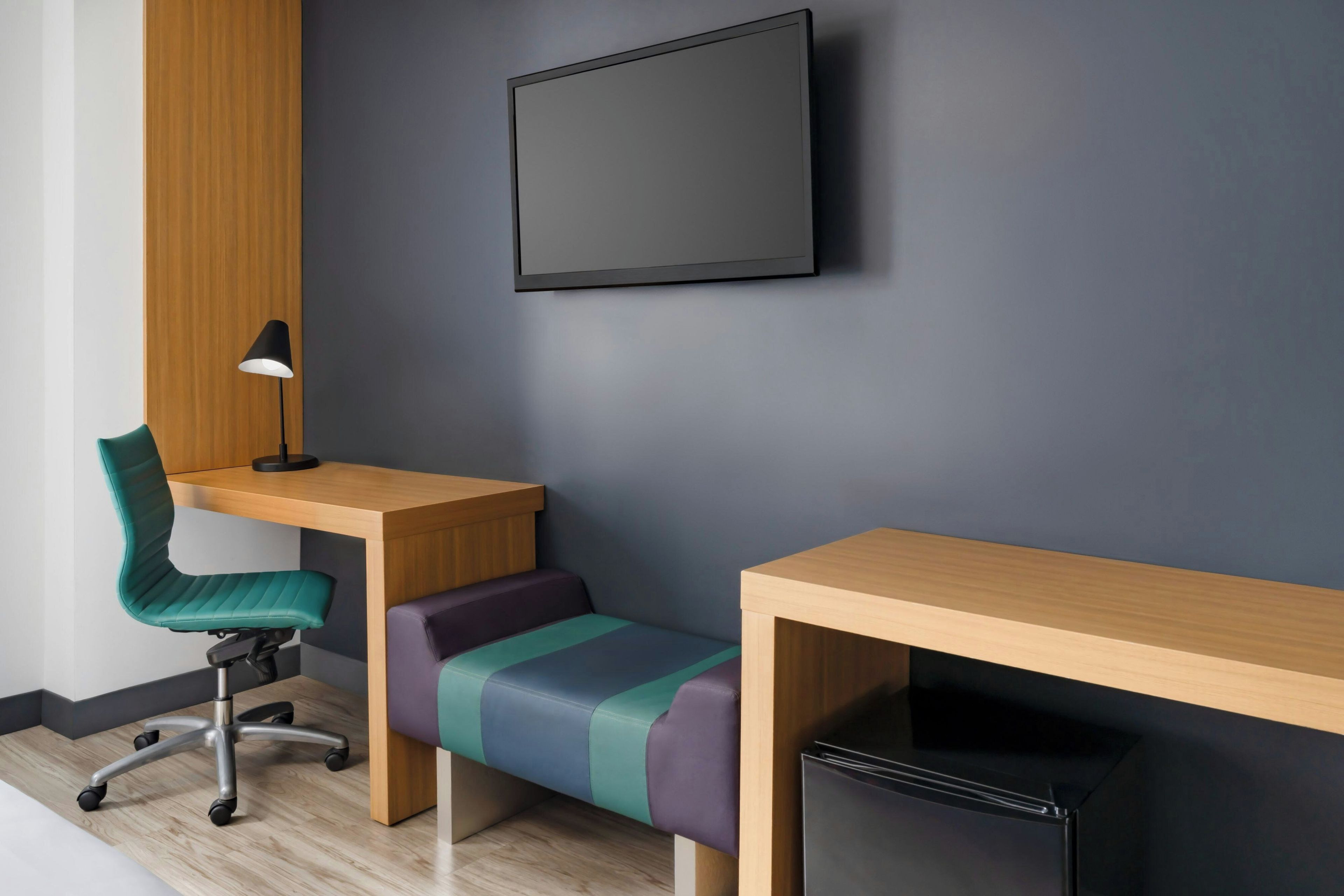 A modern office space with a desk, chair, bench, and a black monitor.