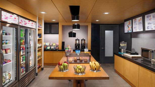 Un área de cocina moderna con una mesa de madera, un refrigerador, una cafetera y un microondas.