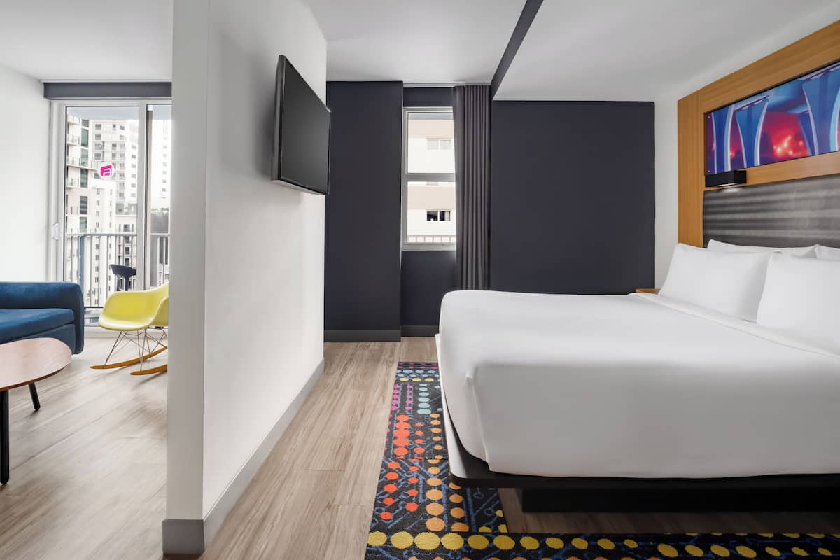 A hotel room with a bed, a TV, a window, a balcony, and a seating area with a table and chairs.