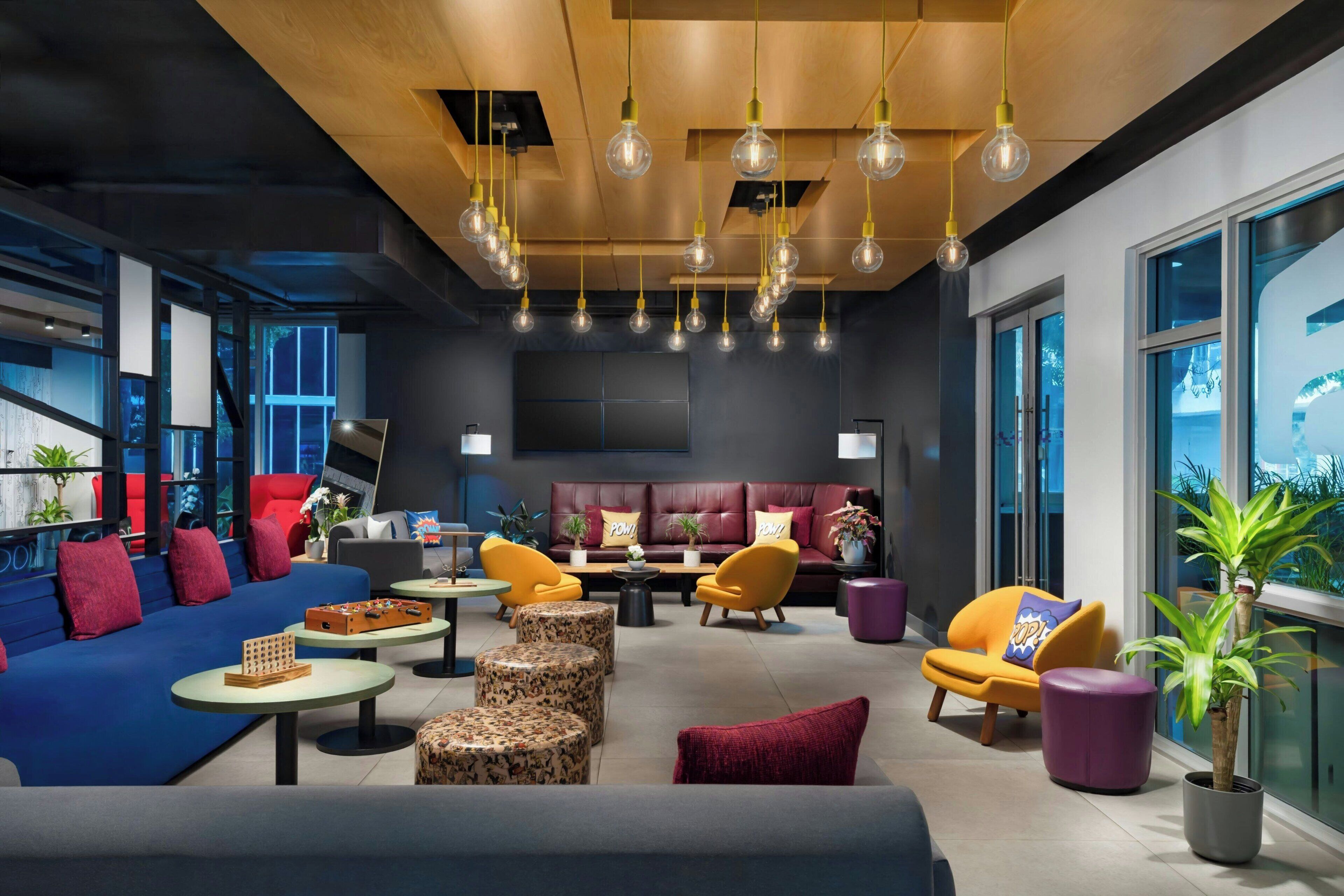 Un espacio lounge moderno con sofá, sillones, una mesita de centro y un área de descanso con un sofá rojo y cojines.