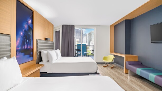 A hotel room with a large bed, a sofa, a TV, a balcony with a view of buildings, and a chair. - Aloft by Marriott Miami - Brickell (Miami)