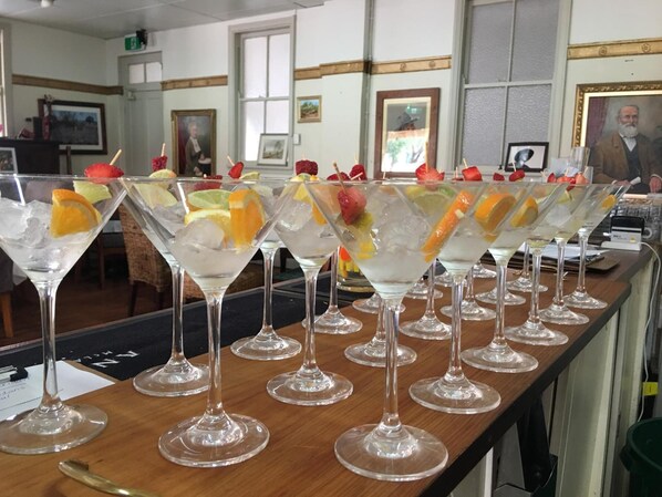 A bar area with multiple martini glasses filled with a clear liquid and garnished with fruits, set on a wooden counter.