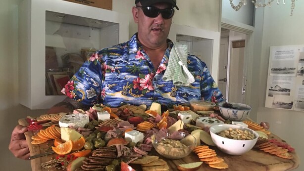 Un homme tenant une grande planche en bois sur laquelle sont disposés divers fromages, viandes et fruits.
