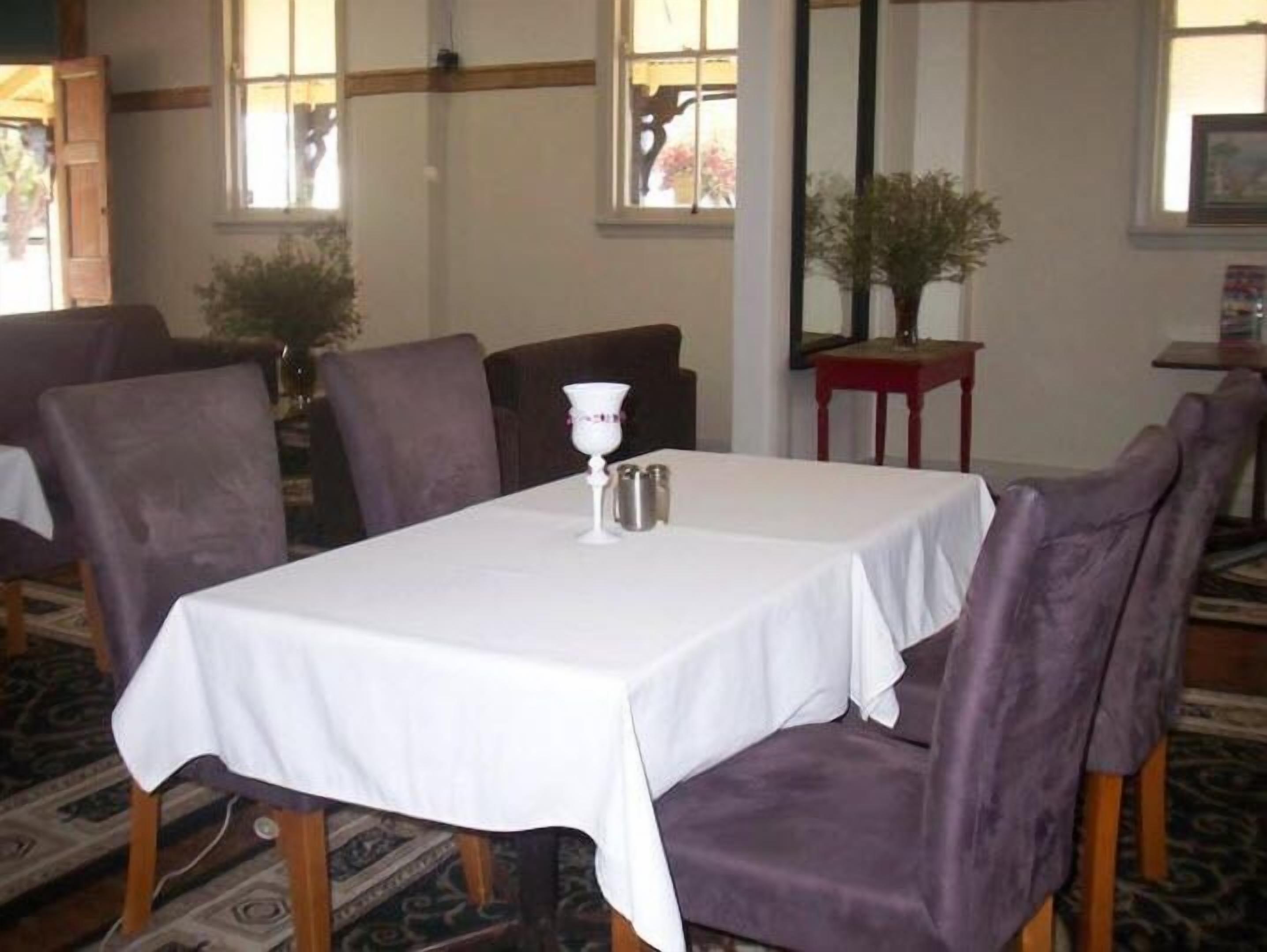 Een eetgedeelte met een witte tafel, paarse stoelen en een kleine potplant.