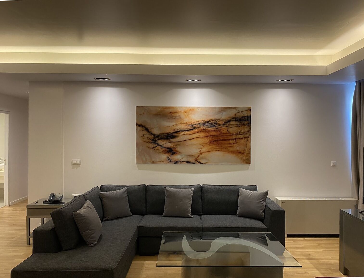 A modern living room with a sectional sofa, a glass coffee table, and a large abstract painting on the wall.
