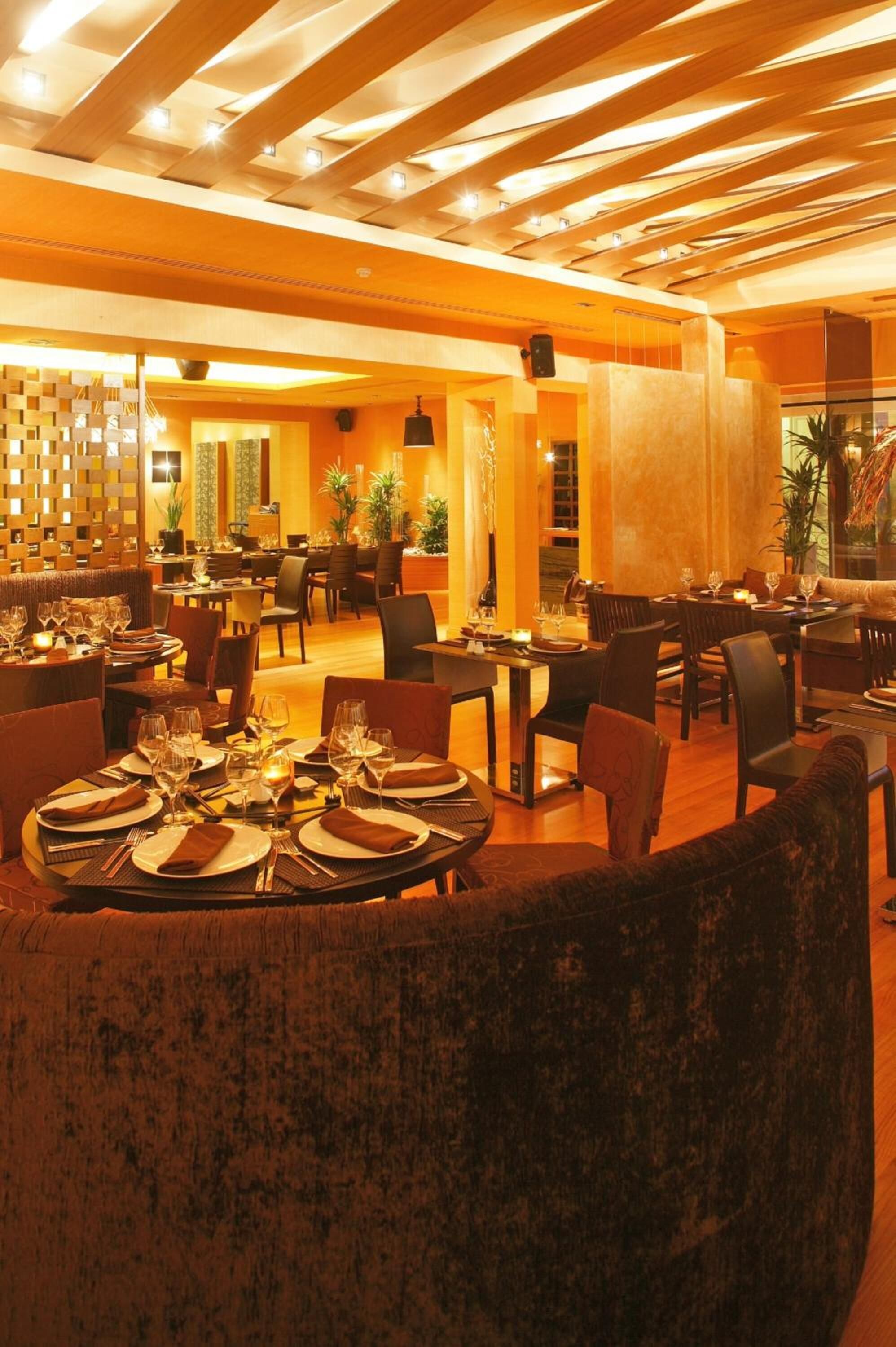 Un ristorante con tavoli rotondi apparecchiati per la cena, travi in legno al soffitto e un'illuminazione calda.