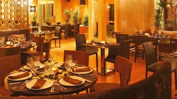 Un ristorante con tavoli rotondi apparecchiati per la cena, travi in legno al soffitto e un'illuminazione calda.