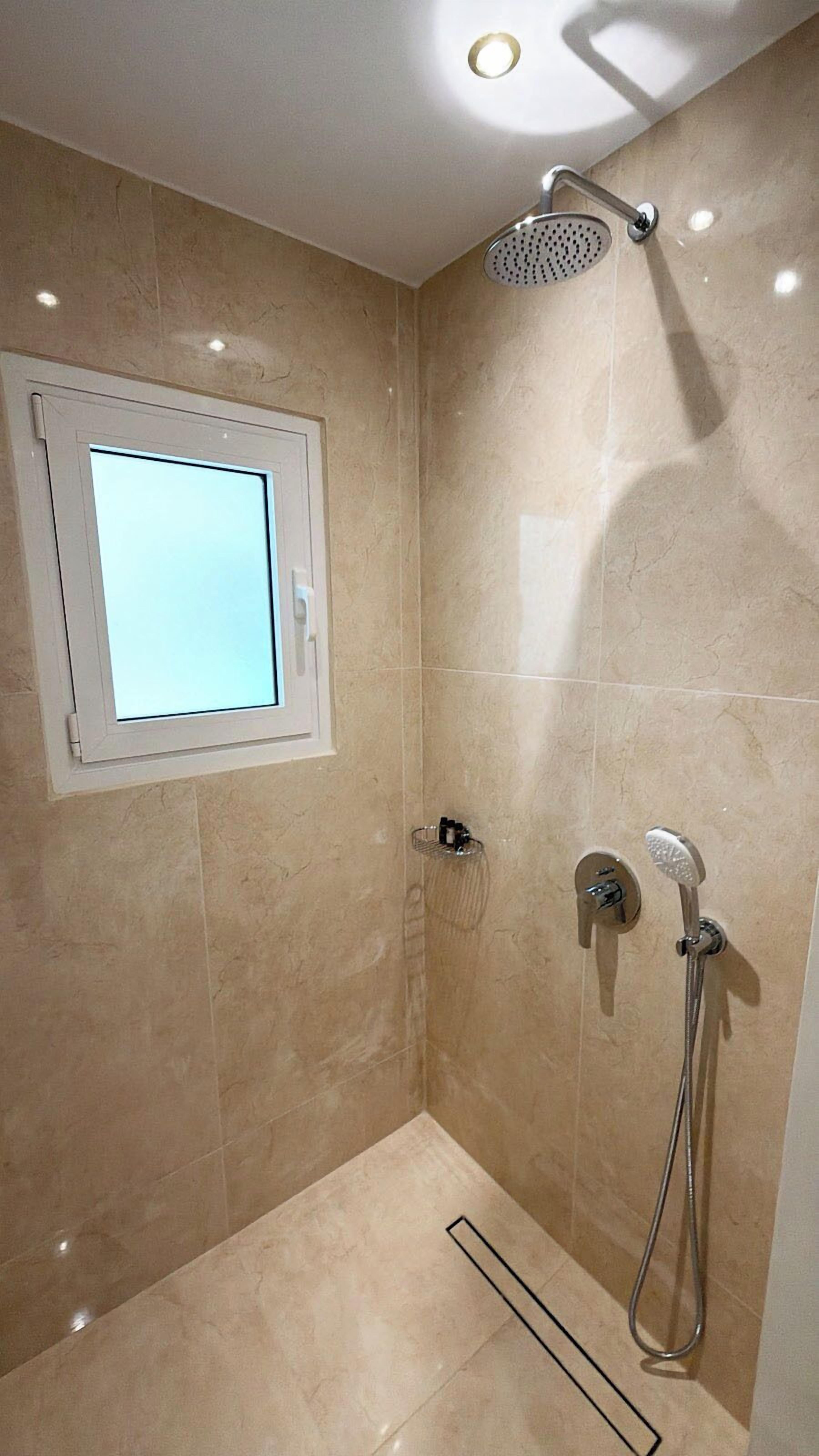 Un baño con ducha, ventana y piso de baldosas.