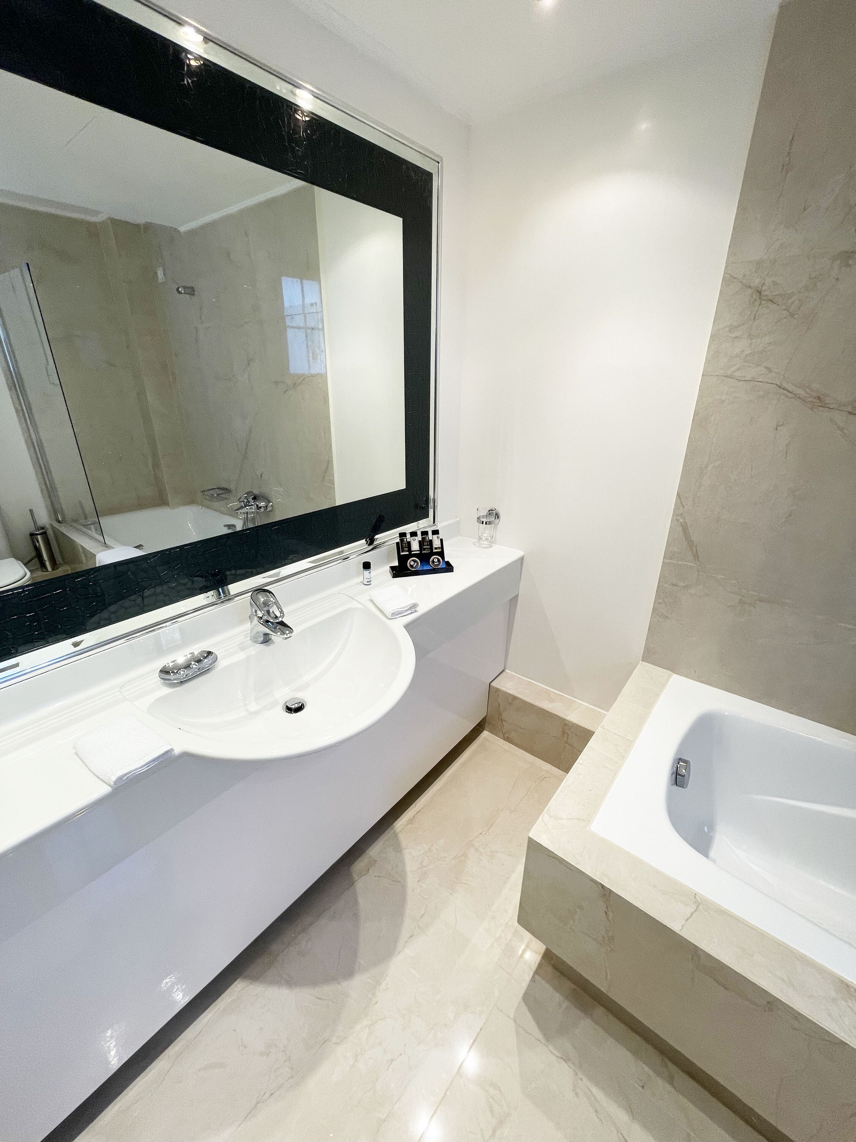 Un baño moderno con un espejo grande, un lavamanos blanco y una bañera.