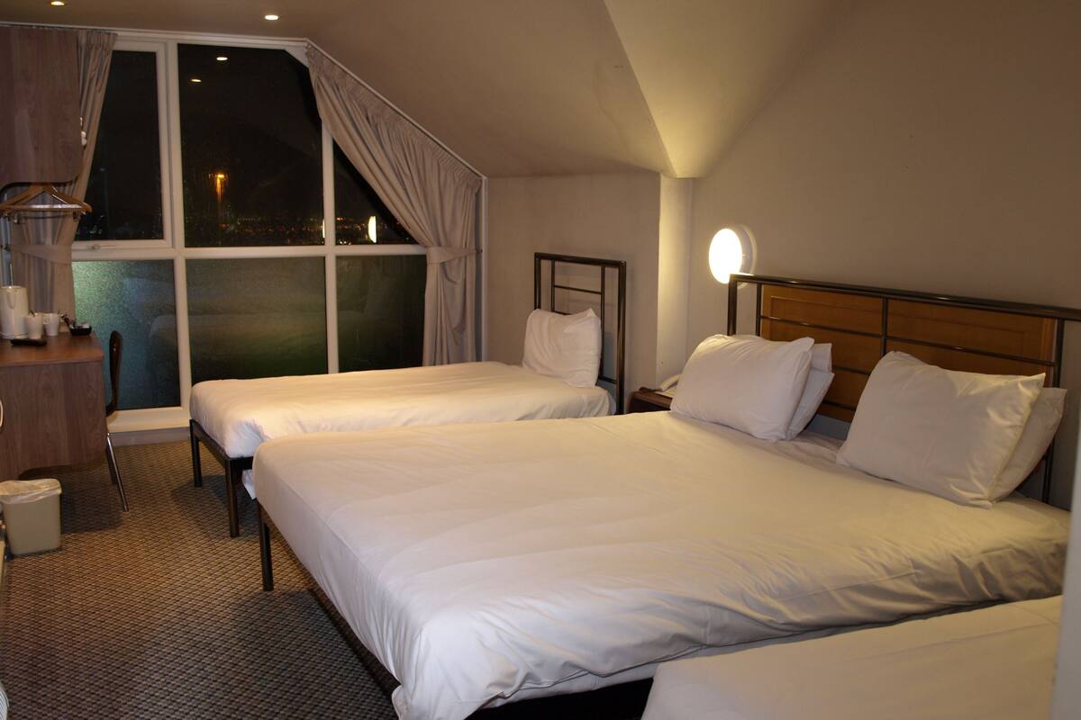 A hotel room with two beds, a desk, and a window with curtains.