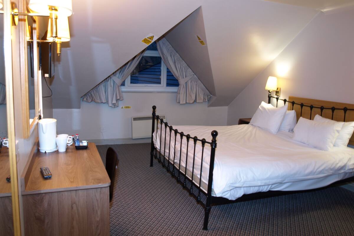 A hotel room with a bed, bedside table, lamp, and a window with curtains.