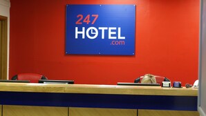 Ein Empfangstresen mit einem Schild, auf dem '247 HOTEL .com' steht, an einer roten Wand.