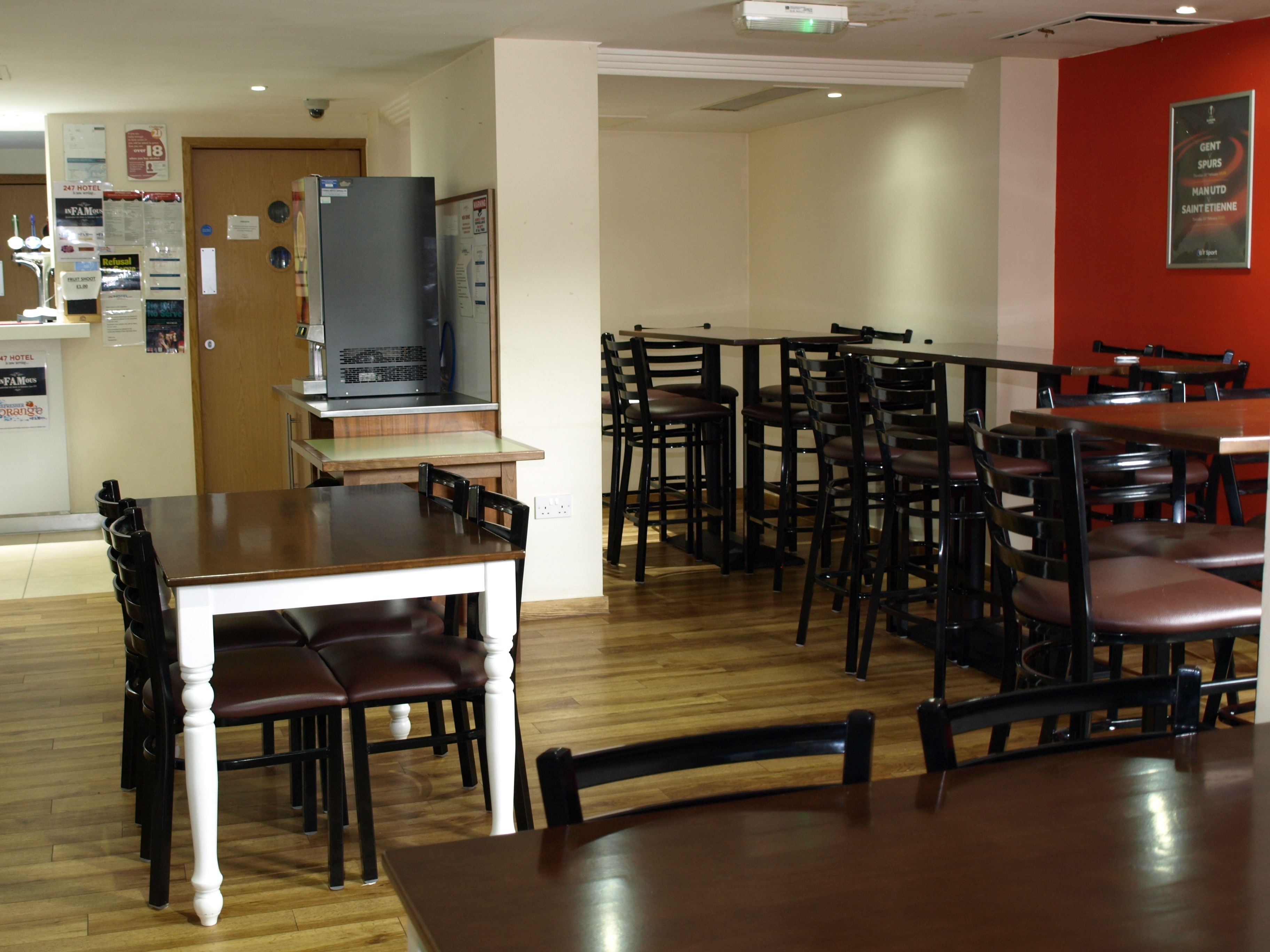 Ein Restaurant mit Holztischen und -stühlen, einem Fernseher und einer roten Wand als Blickfang.
