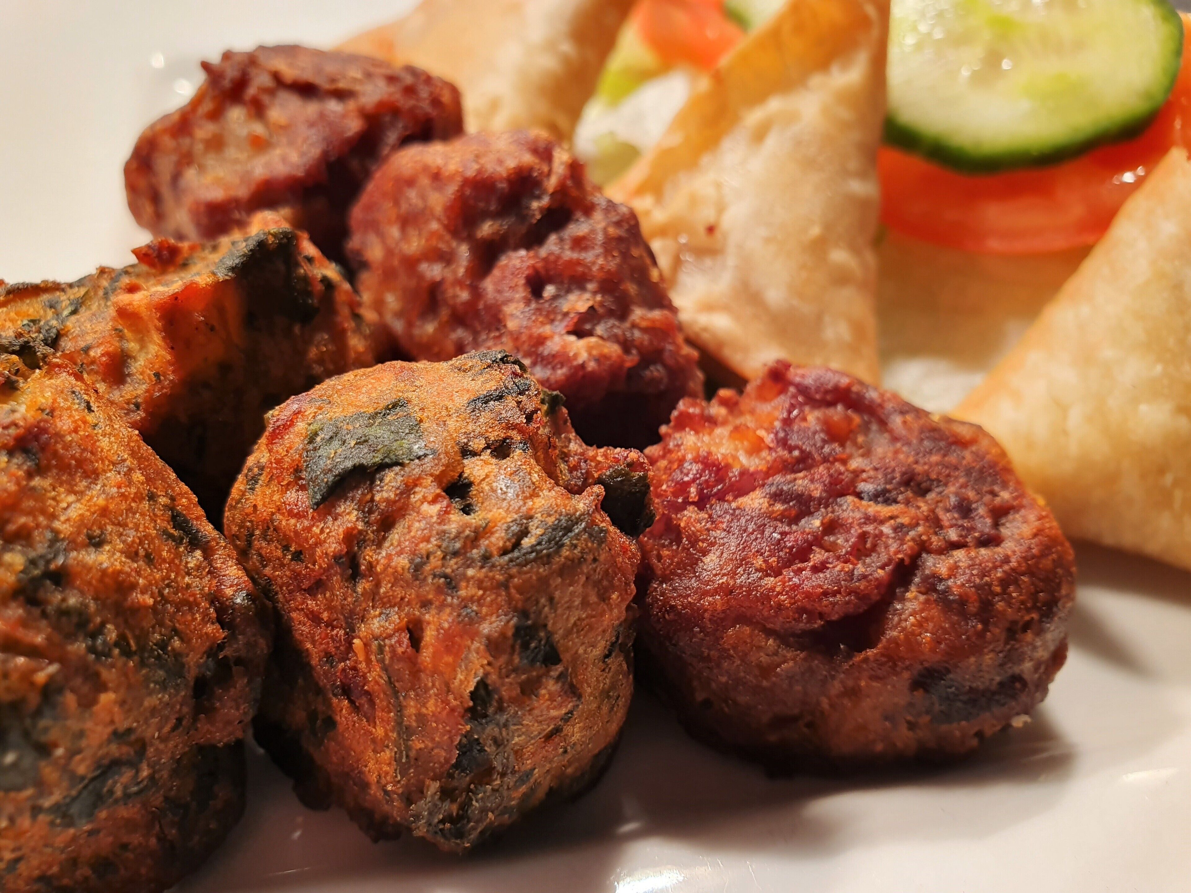 A plate of grilled meatballs with a side of salad and bread.