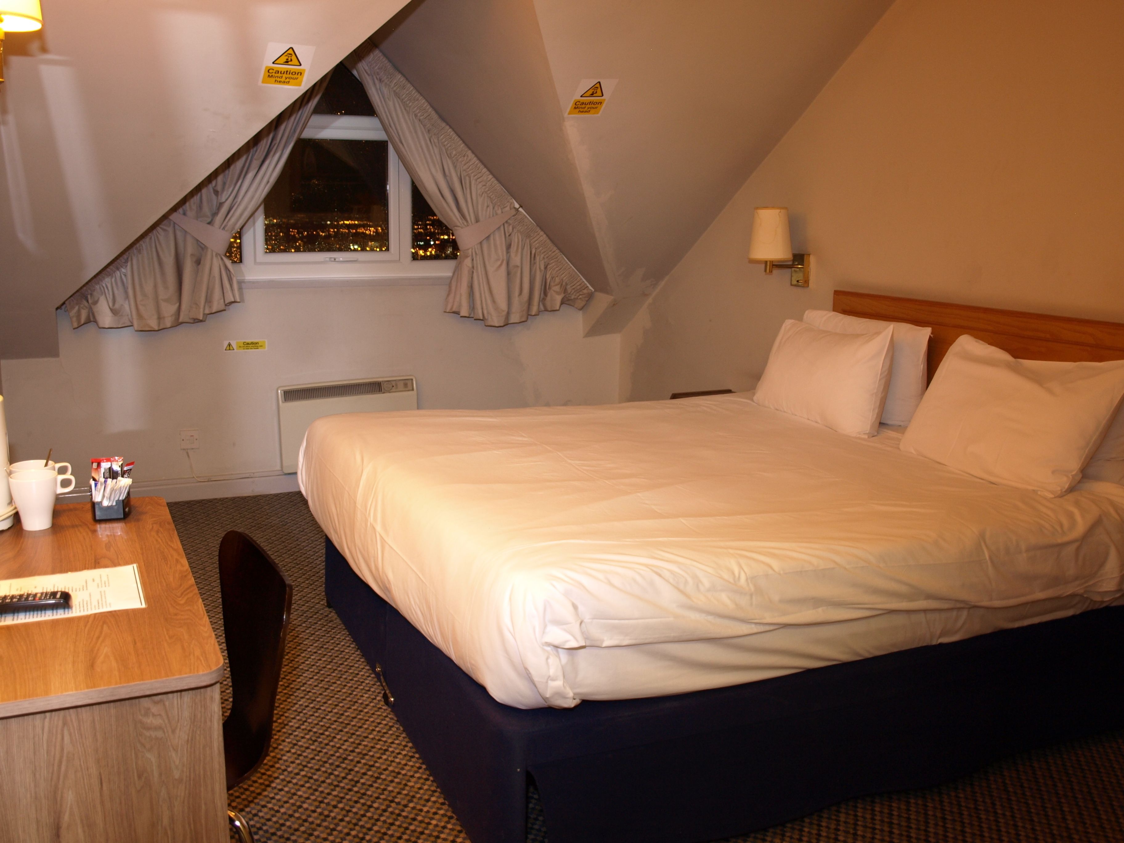 Een hotelkamer met een bed, een bureau en een raam met gordijnen.