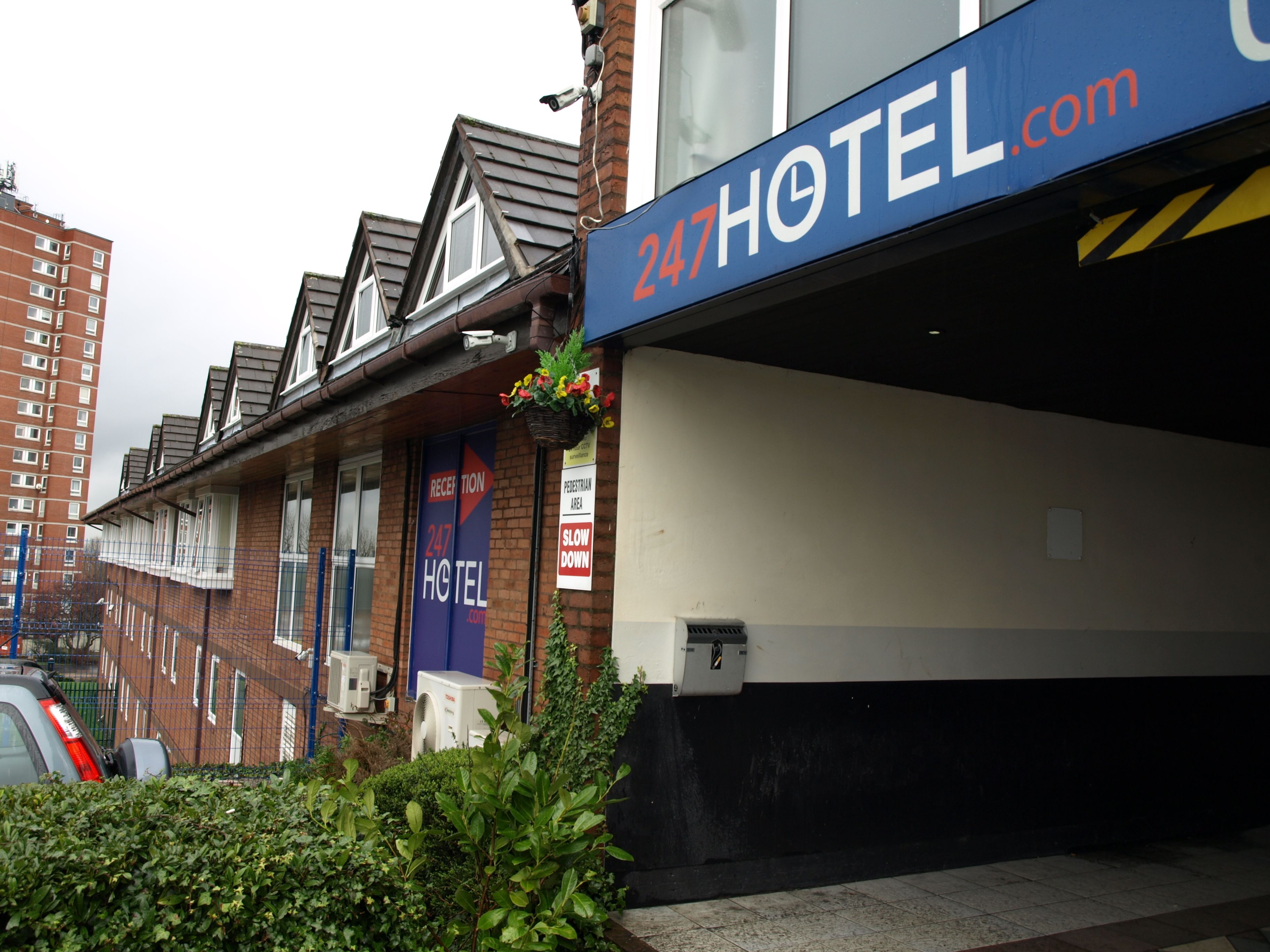 A hotel entrance with a sign reading "247HOTEL.com", a reception area, and a pedestrian area sign.