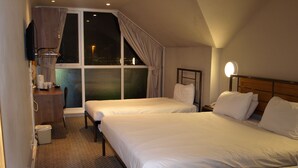 Ein Hotelzimmer mit zwei Betten, einem Schreibtisch, einem Stuhl und einem Fenster mit Vorhängen.