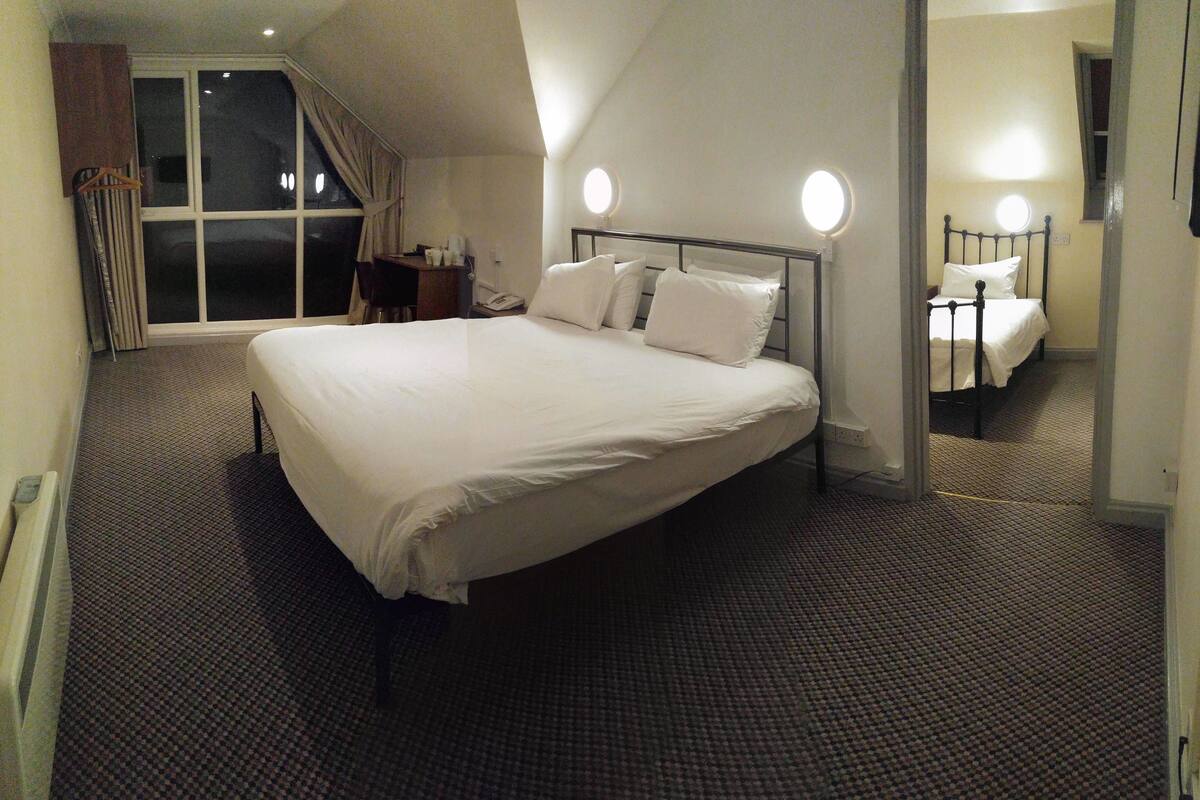 A hotel room with a large bed, a window, a desk, and a chair.
